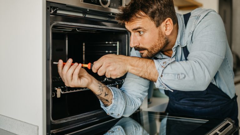 Eine Person in einem Blaumann schraubt an einem Elektroherd.