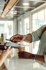 Eine Person h&auml;lt ihr Smartphone an das Kartenleseger&auml;t in einem Caf&eacute;.